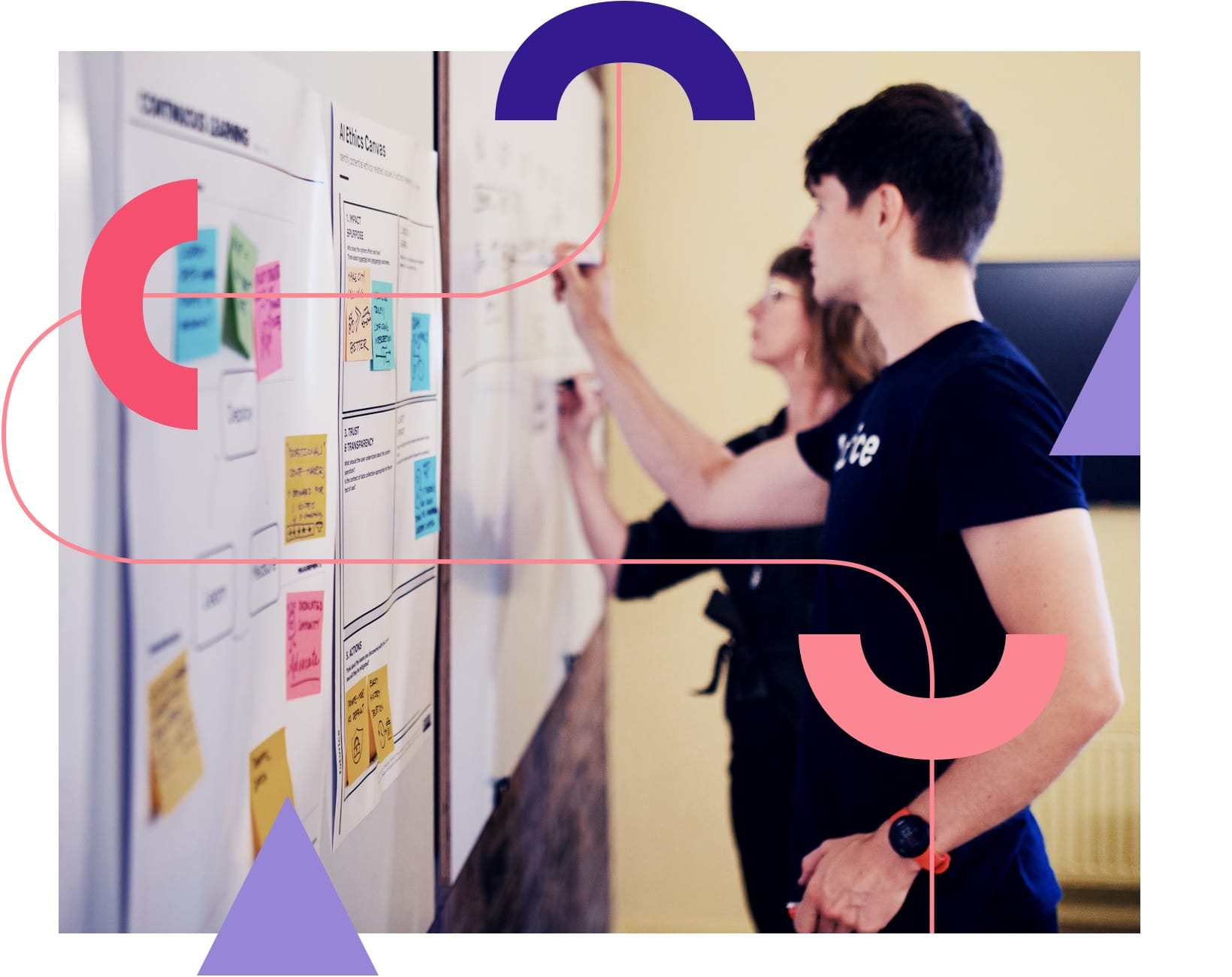 Two people reviewing a whiteboard with colourful sticky notes, overlaid with purple and pink geometric shapes.