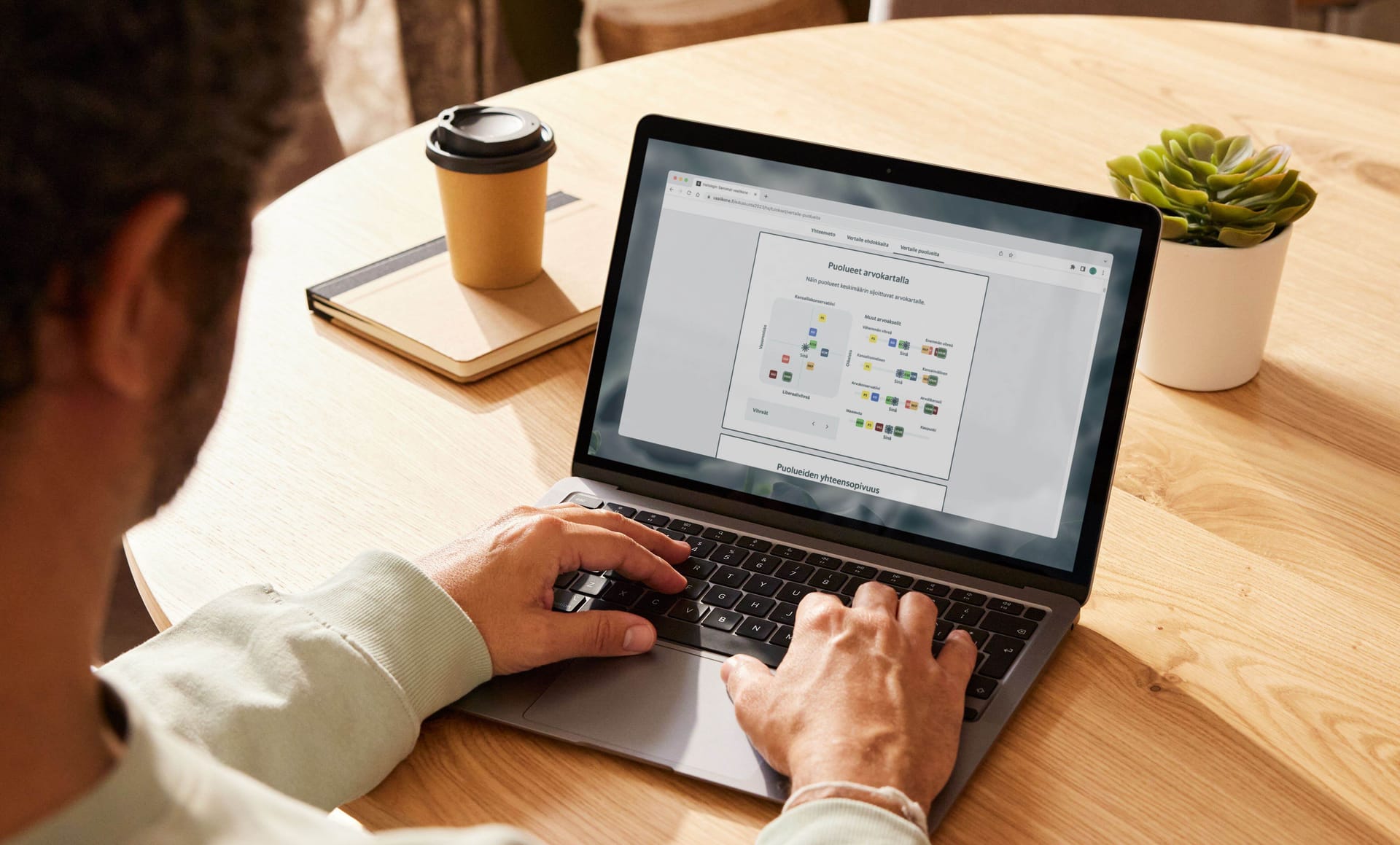Person typing on laptop displaying a website dashboard, with coffee cup and small succulent plant on wooden desk.