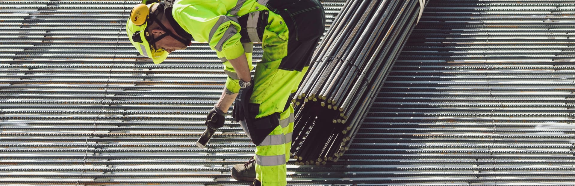 Construction worker in high-visibility clothing working with metal rebar on a construction site.