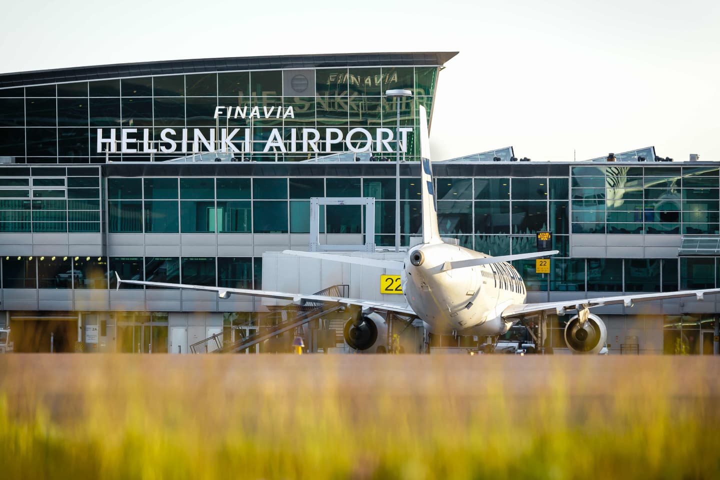 Finnair aircraft parked at Helsinki Airport terminal with glass facade and "HELSINKI AIRPORT" signage visible above gate 22.