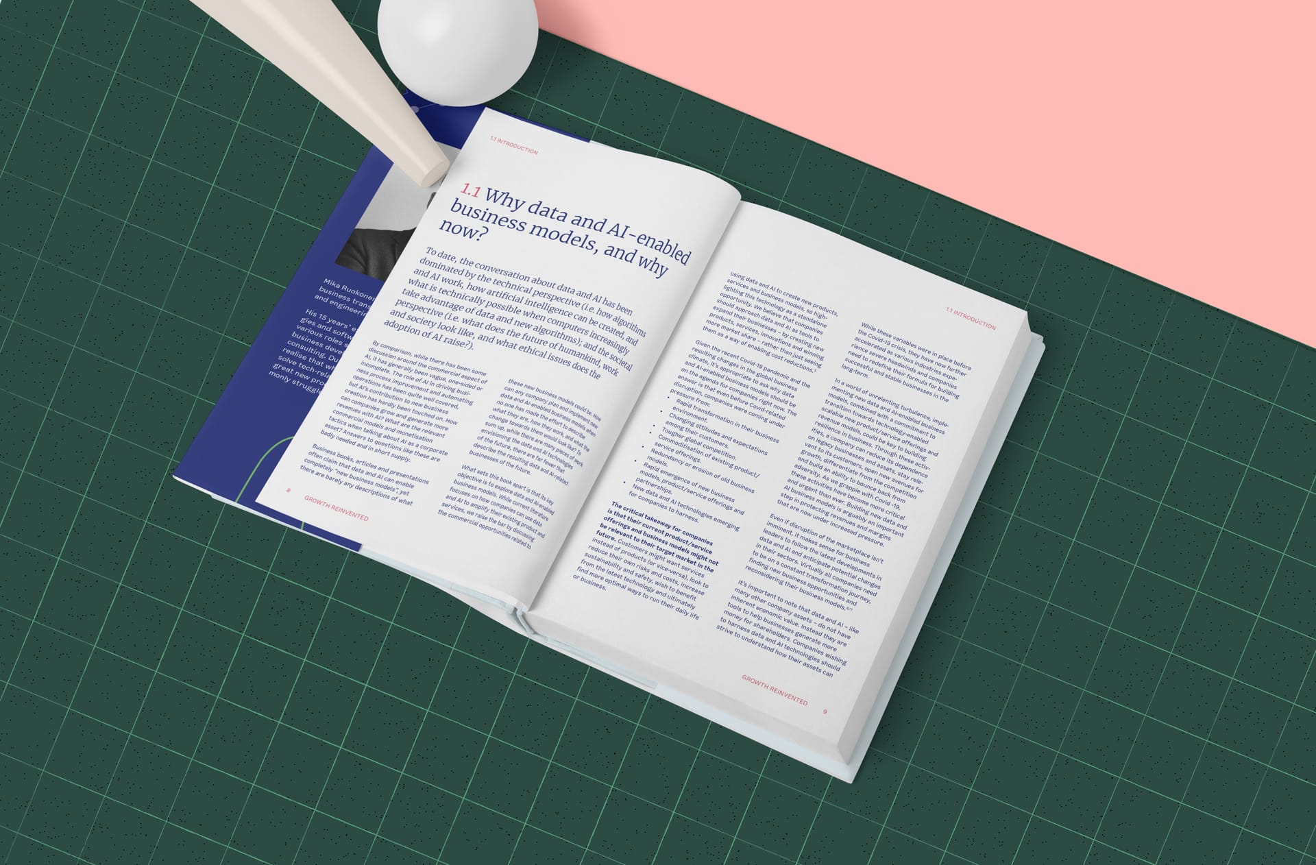 Open book about data and AI-enabled business models on green cutting mat with pink and white design elements nearby.