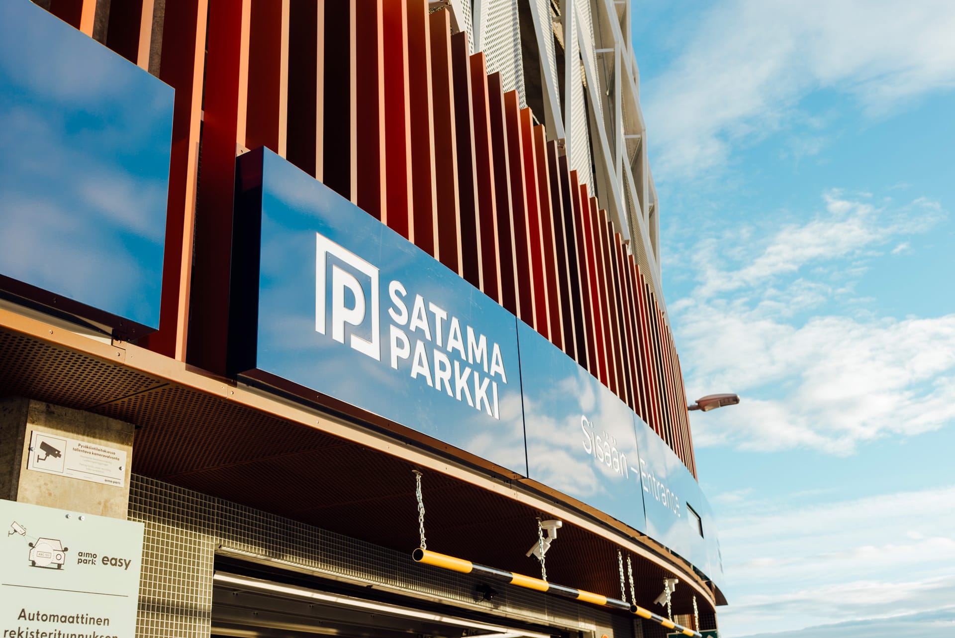 Modern Satama Parkki car park entrance with red vertical slats and blue signage against a bright sky.